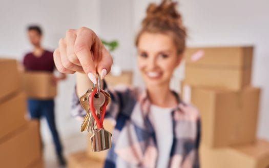 Une femme vendant son bien en copropriété tenant une clé devant des cartons de déménagement.